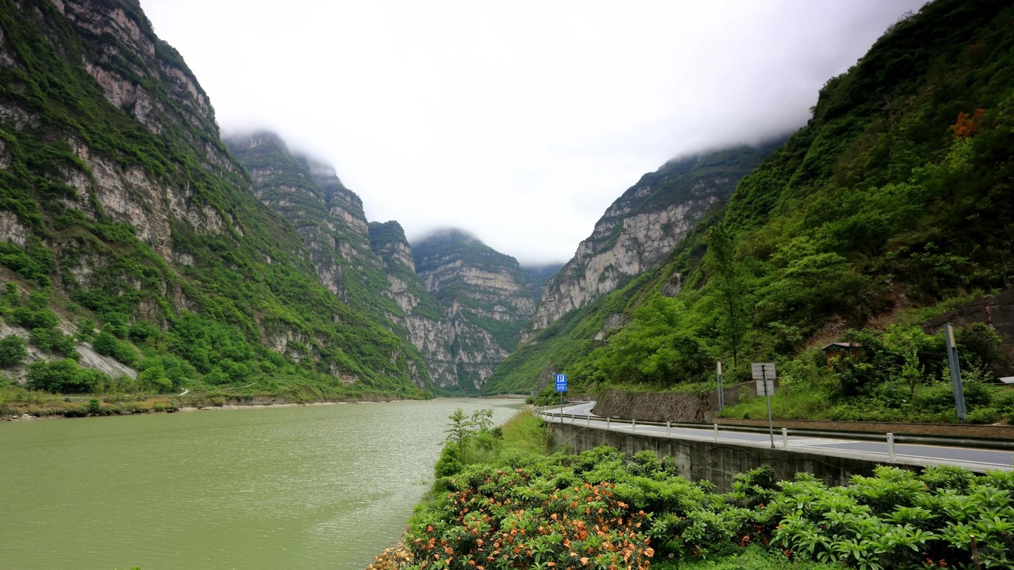 The Dadu River winding green between steep forested canyon walls beside a mountain road.