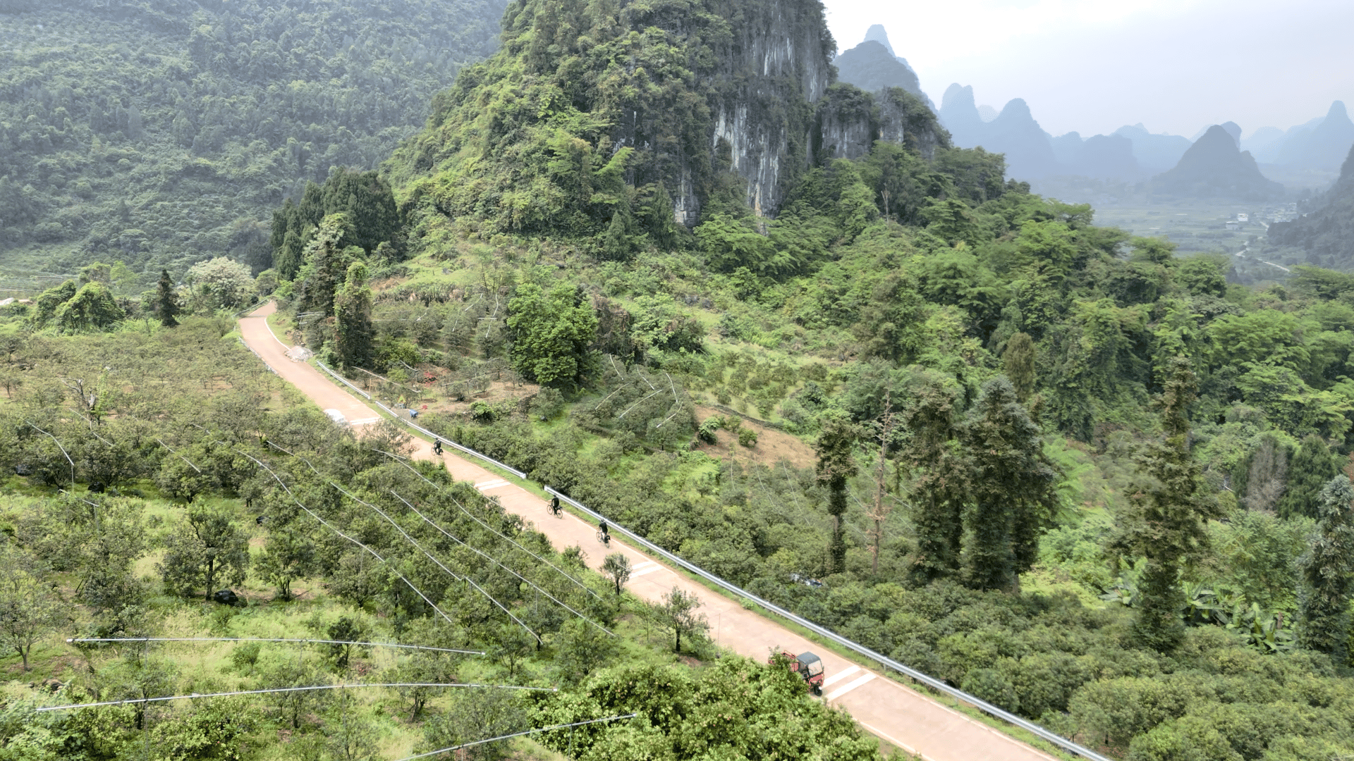 Aerial view of riders on a rural road below a limestone cliff in Yangshuo
