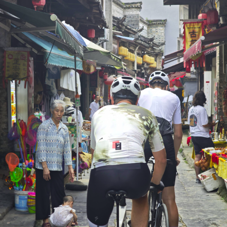 Two cyclists in professional gear riding through the traditional market street of Daxu Ancient Town