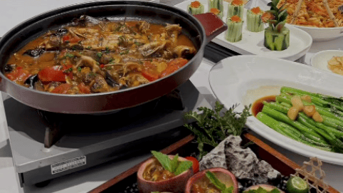 A person using chopsticks to eat authentic Chinese cuisine including spicy braised fish, bok choy, and passion fruit