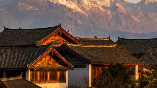 Traditional Chinese architecture in Lijiang Old Town with Jade Dragon Snow Mountain at sunset.