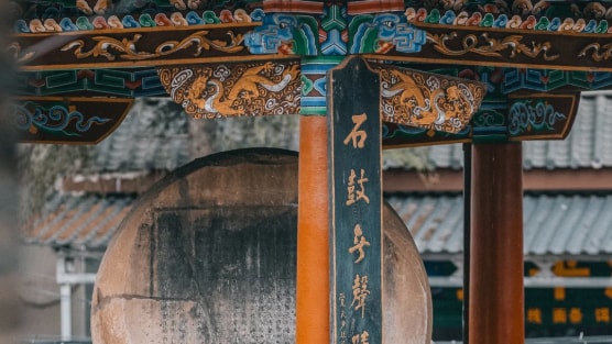 Ornate Chinese temple architecture featuring a stone drum and calligraphy inside a colorful pavilion.