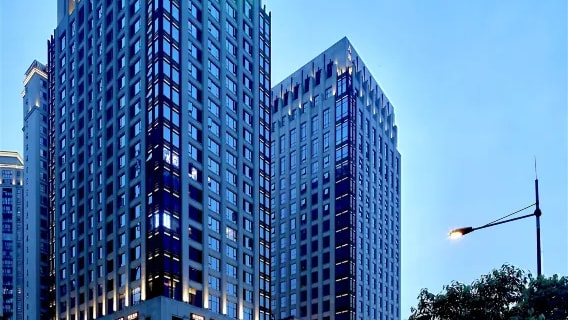 The glass facade of Chengdu Yuandao Hotel above a city street at dusk.