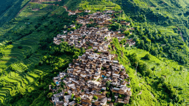 Aerial view of a traditional stone mountain village surrounded by lush green terraced rice fields.