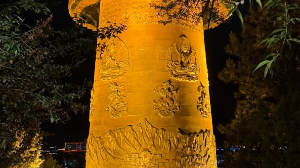Illuminated golden giant prayer wheel in Shangri-La, China at night with intricate carvings.