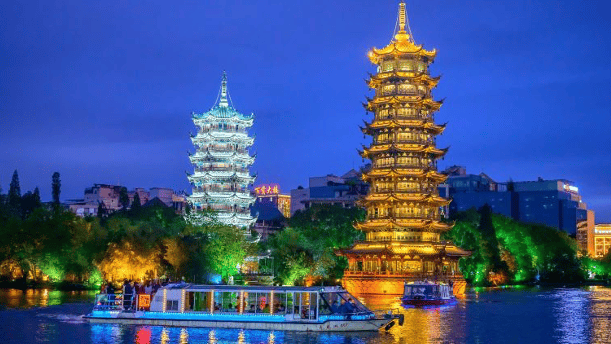 Illuminated Sun and Moon Pagodas reflecting on Shanhu Lake with a tour boat in Guilin, China at night.