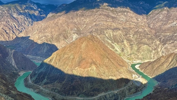 Panoramic view of the First Bend of the Yangtze River winding through a deep mountain valley under a cloudy sky.