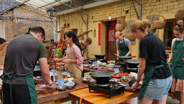 Students prepare traditional recipes in an outdoor Chinese cooking class with woks and fresh ingredients.