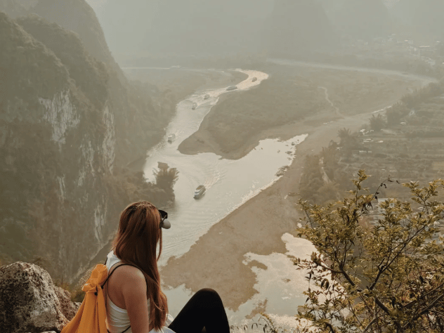Guest seated on a summit rock in hazy light above the river and its sandbars