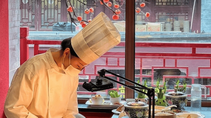 A chef in a white uniform carves a traditional roasted Peking duck at a restaurant table.