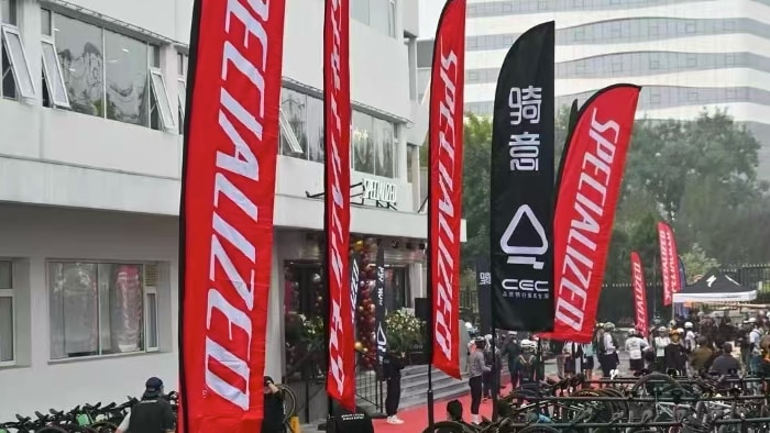 Red Specialized feather flags stand tall above rows of parked bicycles at an outdoor cycling event.
