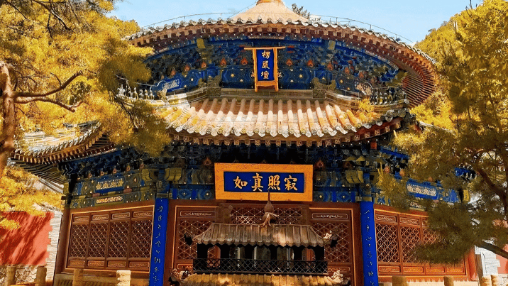 A colorful traditional Chinese pagoda temple with gold and blue details surrounded by autumn trees.