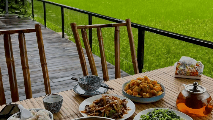 A traditional dinner served on a bamboo table overlooking lush green rice fields in a rural valley.