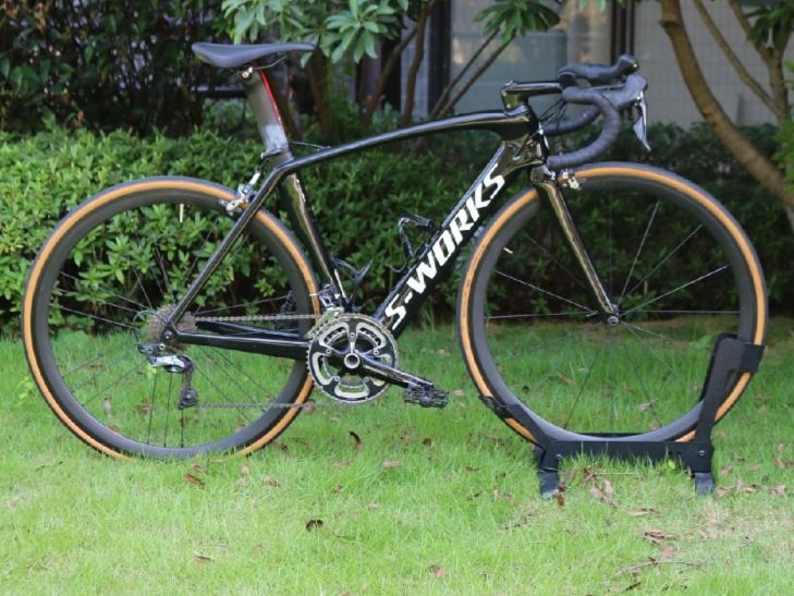 A black Specialized S-Works Venge carbon fiber road bike with tan wall tires parked on a green lawn.