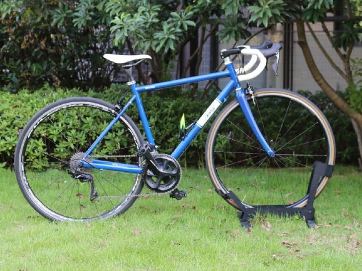 A retro pink road bike with white drop handlebars parked on a green grass lawn.