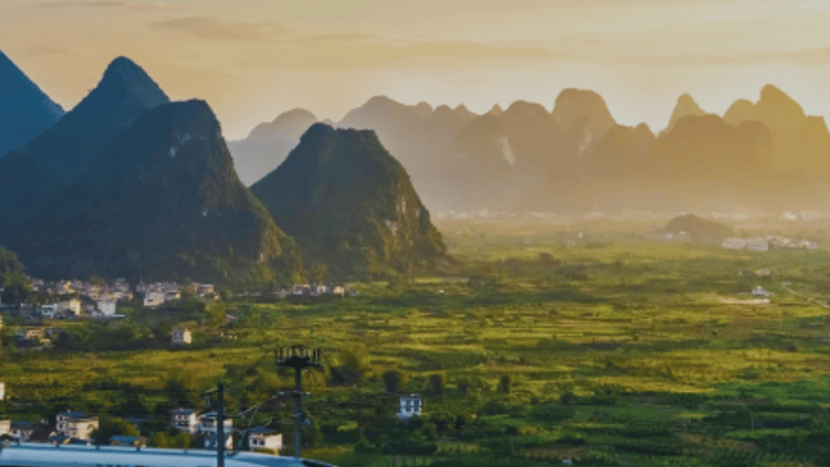 A high-speed train travels across a bridge with a backdrop of karst mountains at sunset in China.