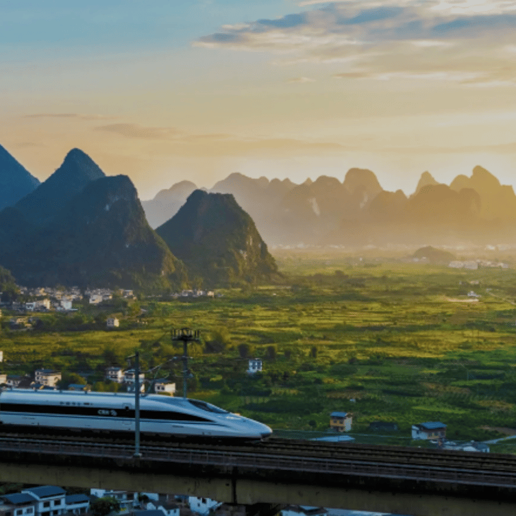A high-speed train travelling across a bridge with a backdrop of karst mountains at sunset near Xingping