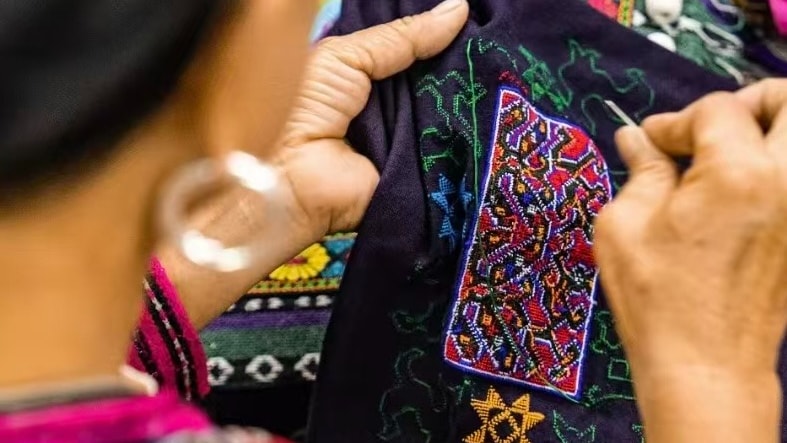 Close-up of an artisan hand-stitching intricate traditional Hmong embroidery on black fabric.