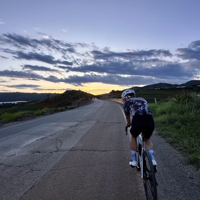 Cyclist on an open lakeside road at dusk under streaks of cloud