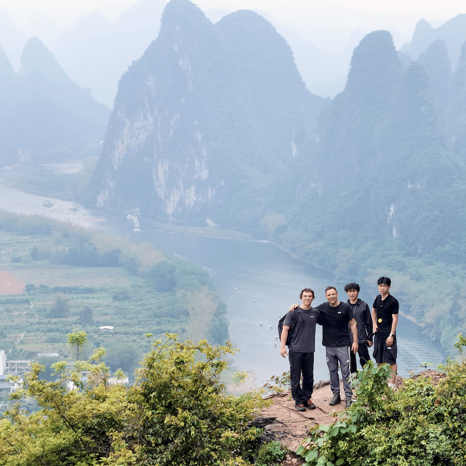 Four riders on a clifftop ledge high above a bend of the Li River