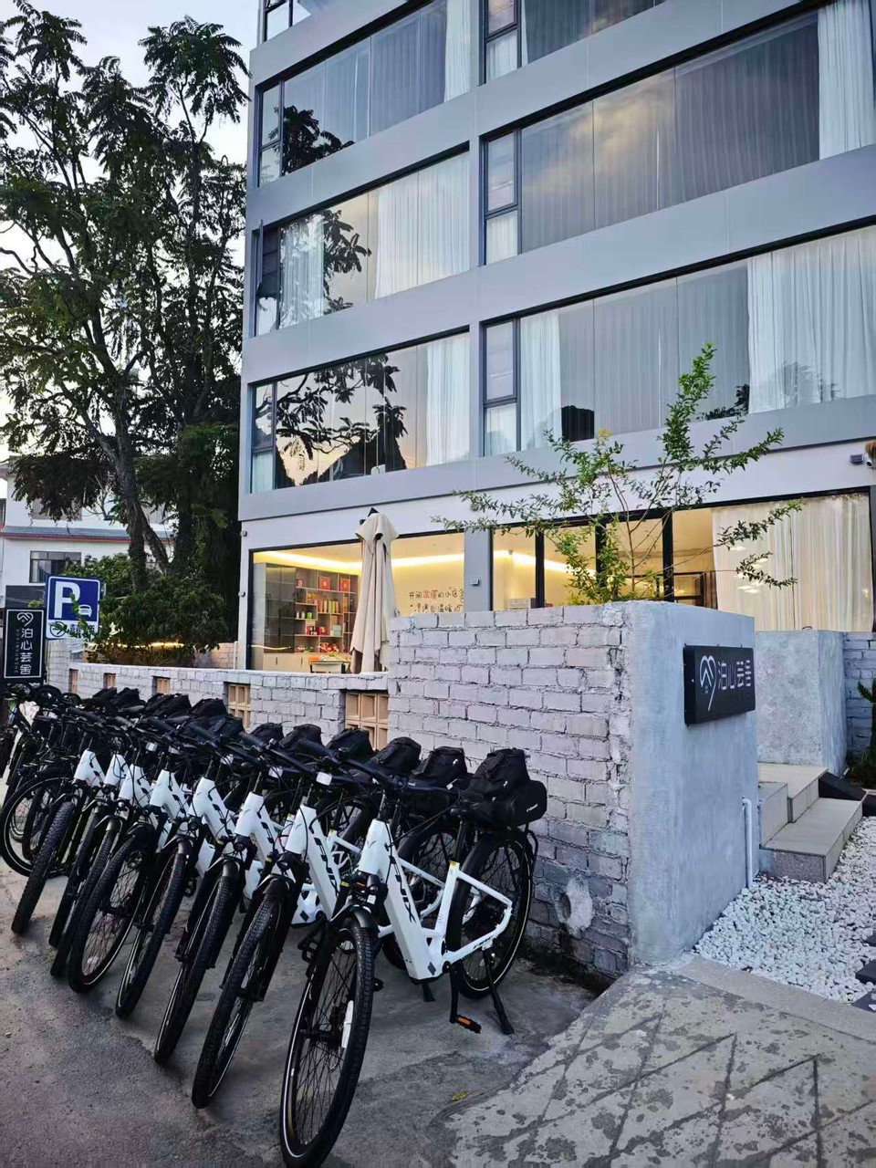 Row of white rental e-bikes with panniers parked outside the CycleQuest China shop in Xiatangzhai, Yangshuo
